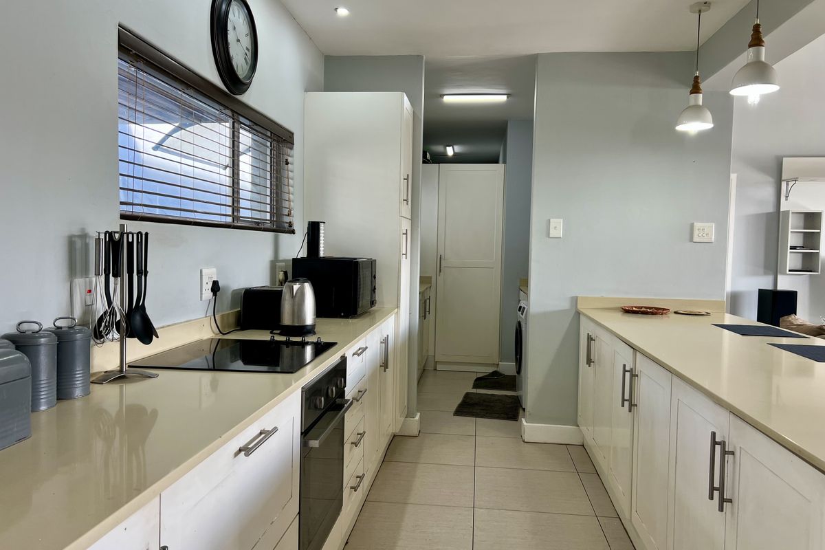 A functional kitchen featuring white cabinetry, stone countertops, integrated hob and oven, and tiled flooring with a clean, modern layout.