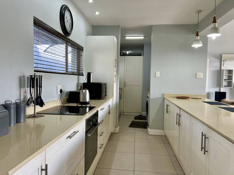 A functional kitchen featuring white cabinetry, stone countertops, integrated hob and oven, and tiled flooring with a clean, modern layout.