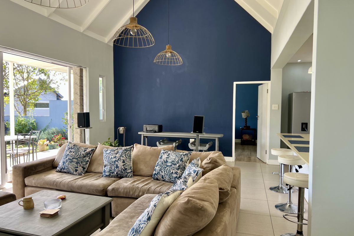 Spacious open-plan living area featuring a dramatic vaulted ceiling, exposed rafters, tiled flooring, and seamless flow to the outdoor patio through large sliding doors.