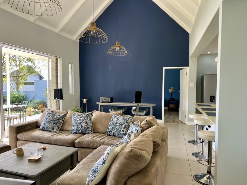 Spacious open-plan living area featuring a dramatic vaulted ceiling, exposed rafters, tiled flooring, and seamless flow to the outdoor patio through large sliding doors.