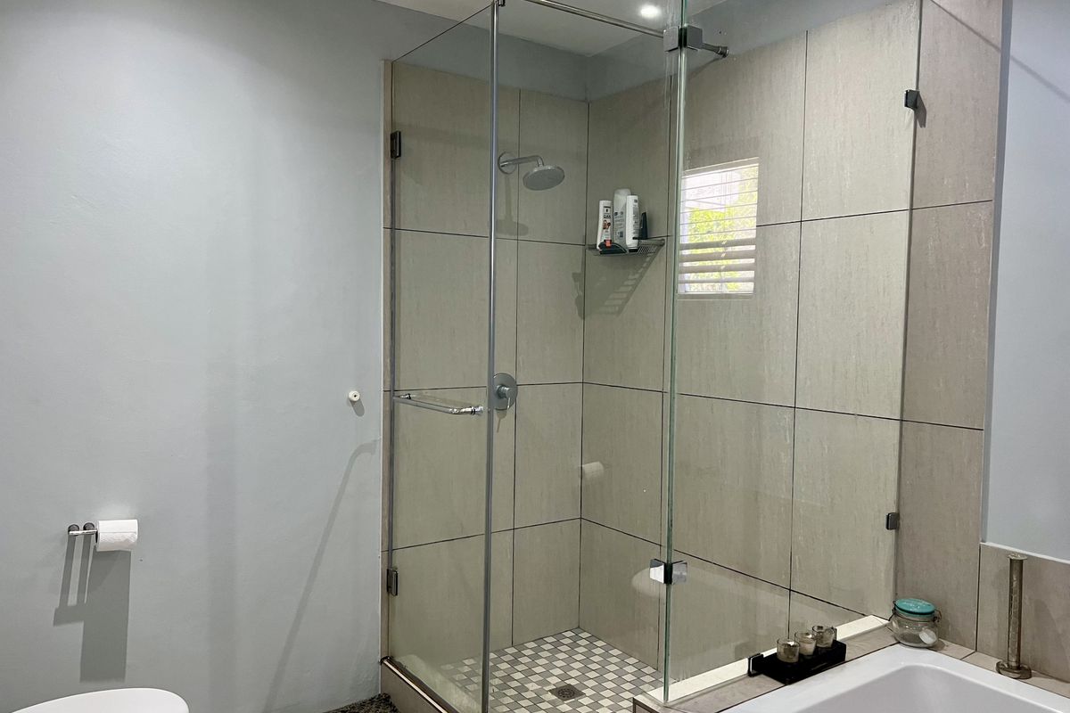A modern bathroom featuring a glass-enclosed shower with mosaic tiling, a built-in bathtub, and neutral wall finishes.