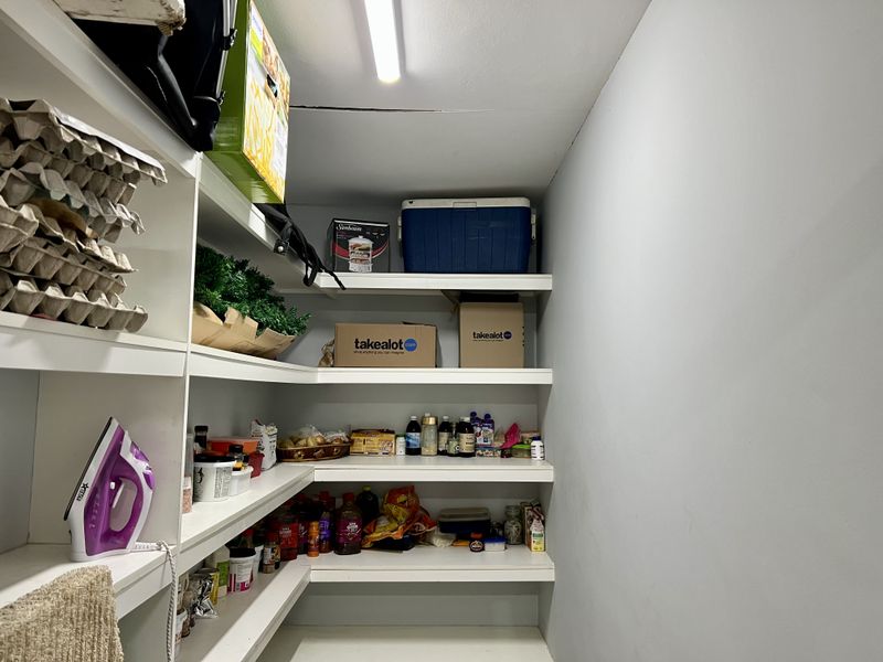 A functional walk-in pantry or scullery area featuring extensive built-in shelving for storage and overhead lighting.