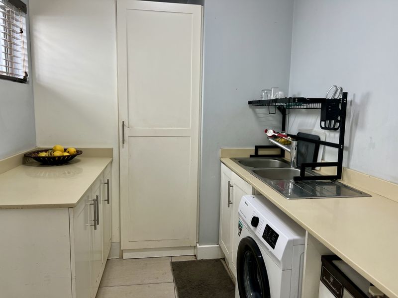 A functional scullery area featuring built-in cabinetry, laminate countertops, a stainless steel double sink, and dedicated space for laundry appliances.