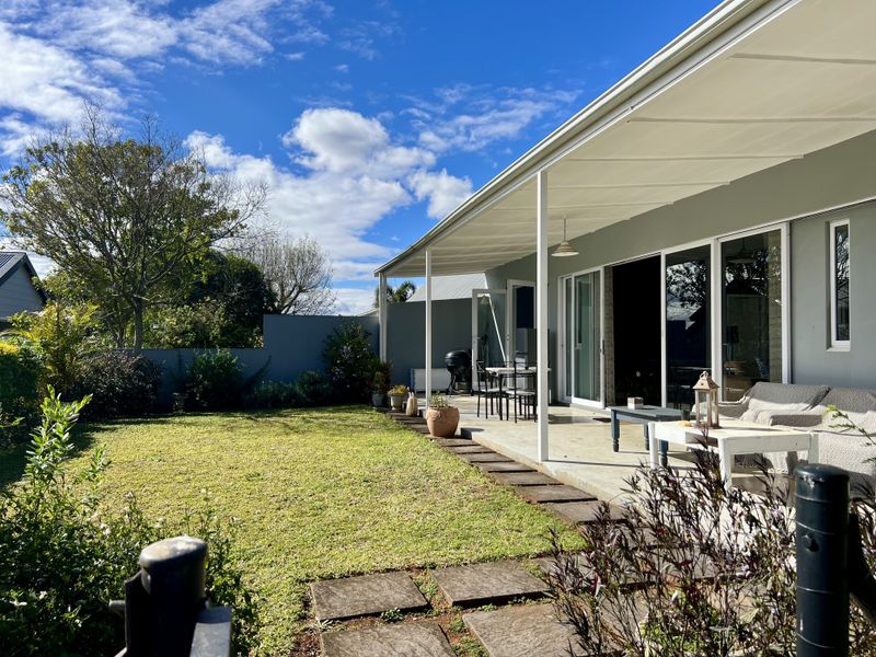 A well-maintained covered patio area featuring concrete flooring and sliding glass doors, overlooking a private garden with a paved pathway.