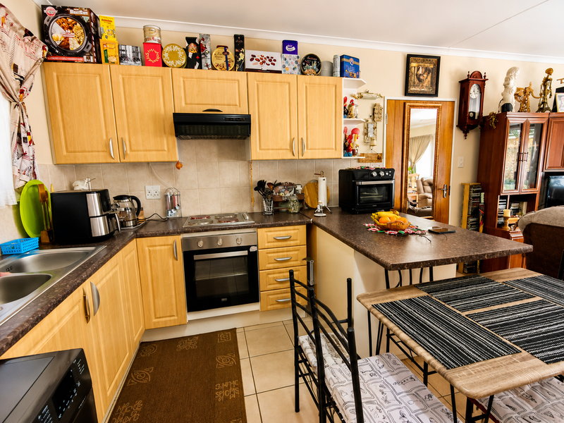Functional kitchen featuring light wood cabinetry, laminate countertops, integrated oven and hob, and a breakfast bar area with tiled flooring.