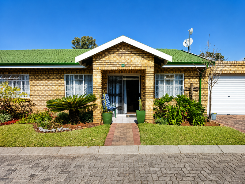 Front elevation of a single-story brick house featuring a green tiled roof, paved driveway, and an integrated garage.