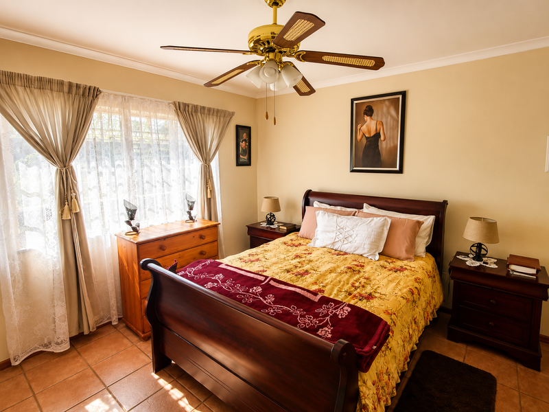 A well-maintained bedroom featuring tiled flooring, a central ceiling fan, and neutral wall tones, offering a comfortable and functional living space.