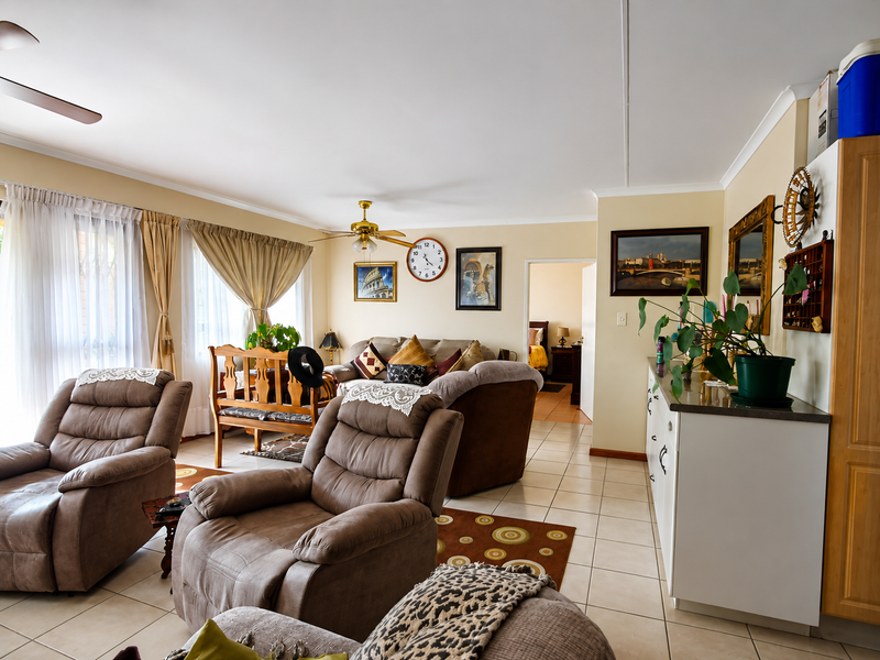 A spacious living room featuring tiled flooring, ceiling fans, and neutral wall tones, offering a comfortable and functional layout for relaxation.
