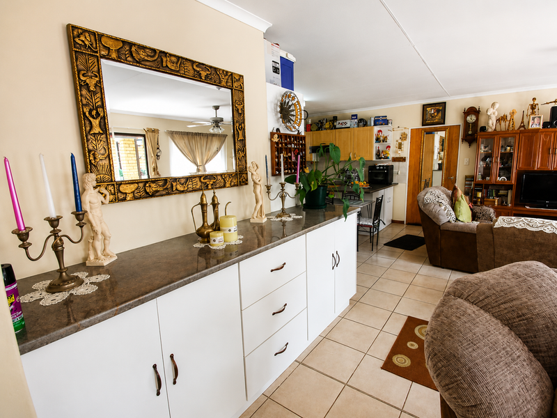 Open-plan living area featuring tiled flooring, a ceiling fan, and built-in cabinetry with a stone-look countertop, seamlessly connecting to the kitchen space.