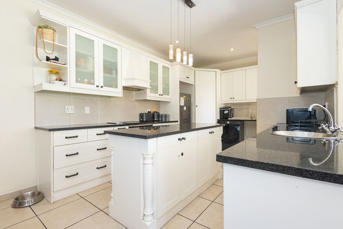 A well-maintained kitchen featuring white shaker-style cabinetry, dark granite countertops, a central island, and ceramic tile flooring with modern pendant lighting.