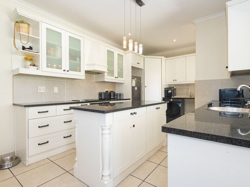 A well-maintained kitchen featuring white shaker-style cabinetry, dark granite countertops, a central island, and ceramic tile flooring with modern pendant lighting.