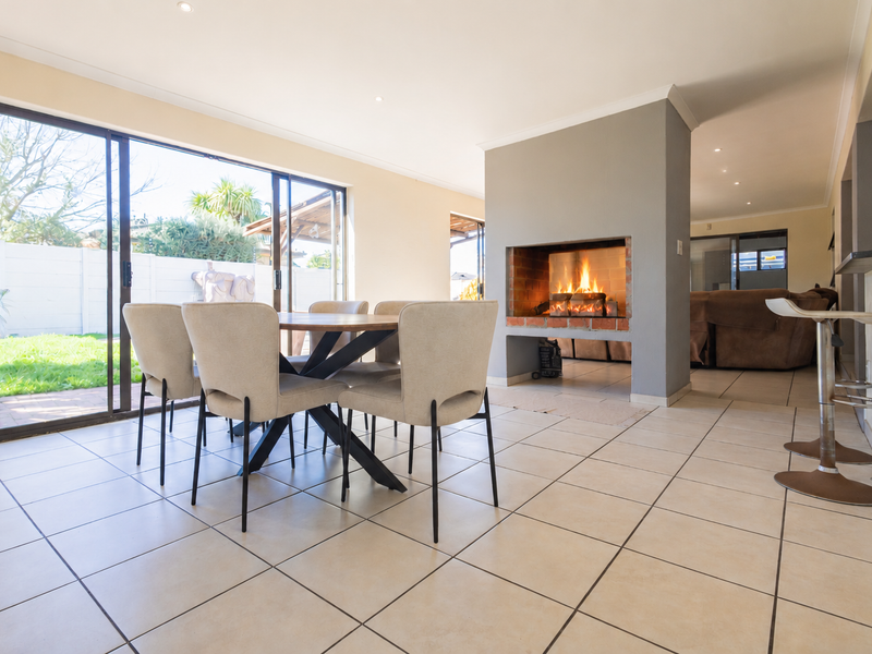 Open-plan living and dining area featuring a central built-in fireplace, tiled flooring, and large sliding glass doors providing direct access to the garden.