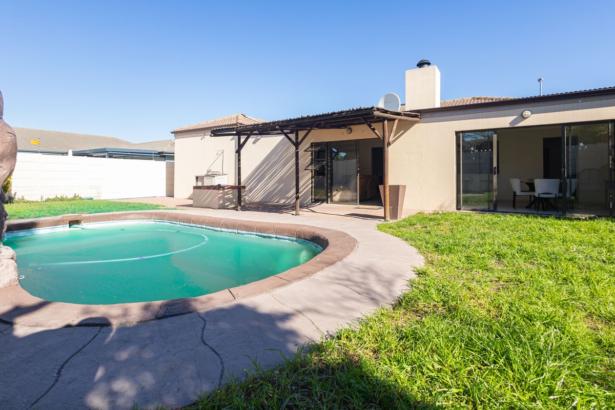 Rear exterior view featuring a swimming pool, a covered patio area with a built-in braai, and direct access to the home via sliding doors.