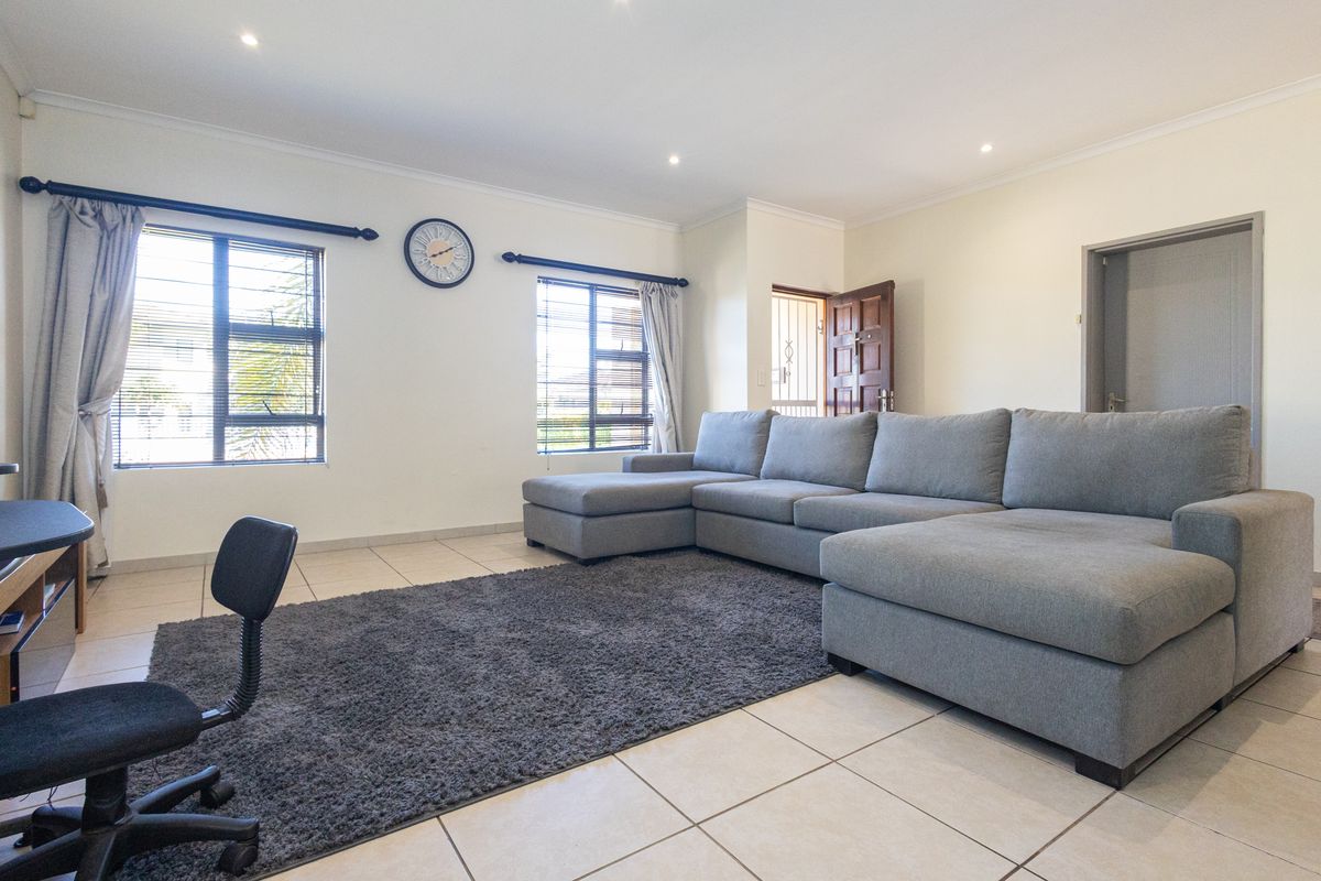 A bright and spacious living room featuring neutral tiled flooring, recessed downlighting, and large windows with security bars.