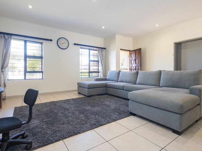 A bright and spacious living room featuring neutral tiled flooring, recessed downlighting, and large windows with security bars.
