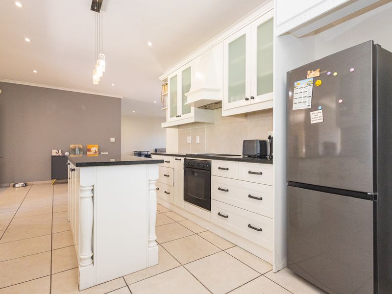 Modern kitchen featuring white shaker-style cabinetry, granite countertops, a central island, and built-in oven with extractor fan, set against tiled flooring.