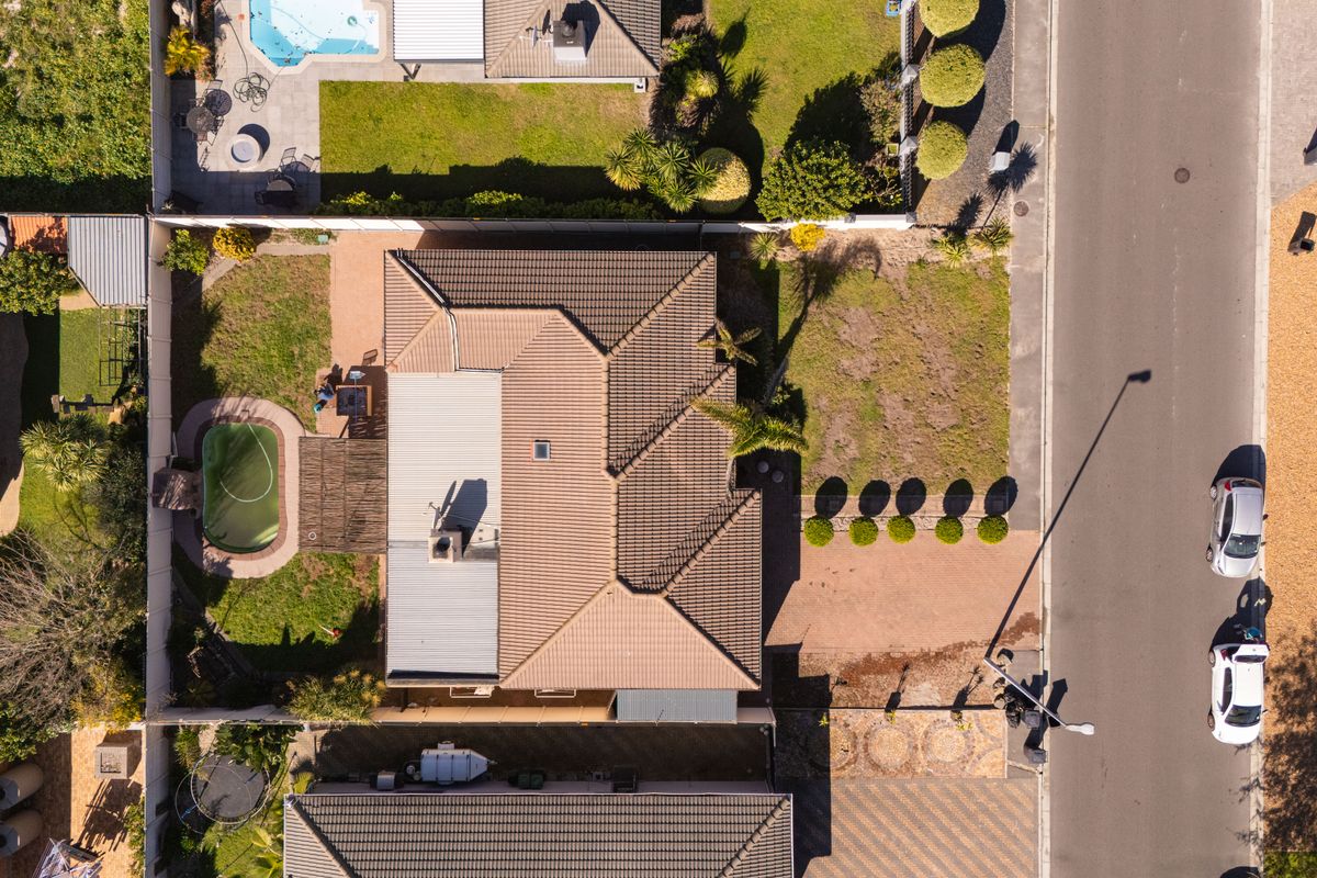 Aerial view of a residential property featuring a tiled roof, private swimming pool, landscaped garden, and paved driveway access from the street.