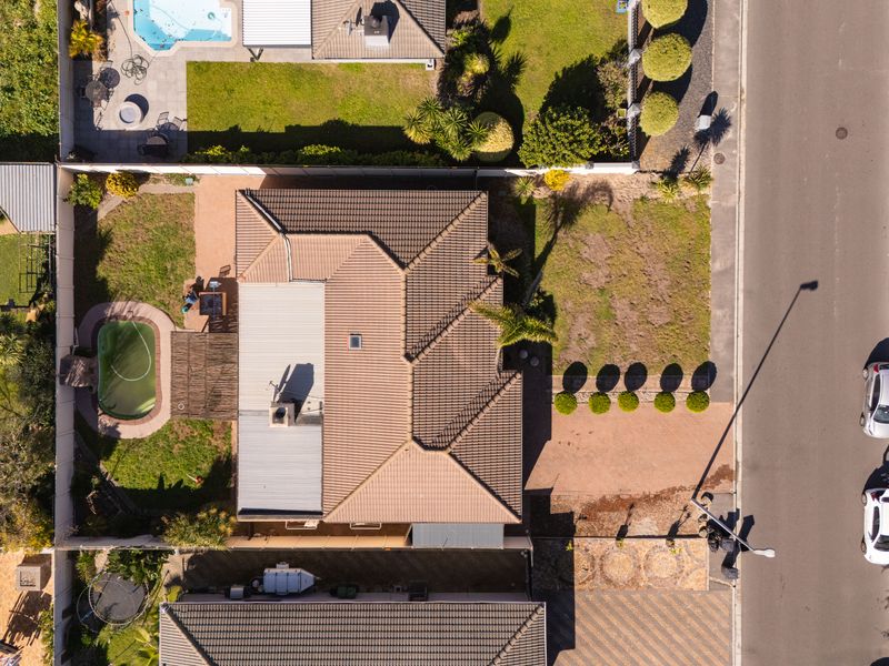 Aerial view of a residential property featuring a tiled roof, private swimming pool, landscaped garden, and paved driveway access from the street.