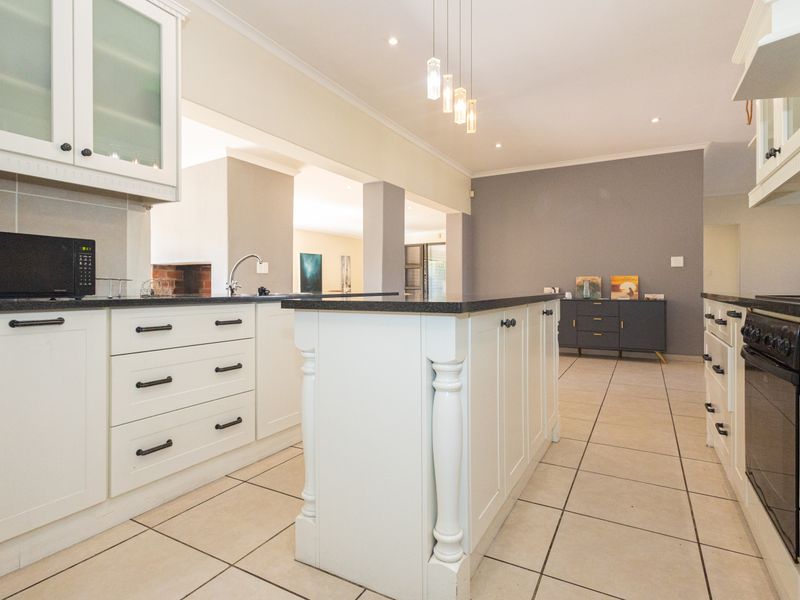 A well-appointed kitchen featuring a central island, stone countertops, shaker-style cabinetry, and integrated oven, flowing into an open-plan living area.