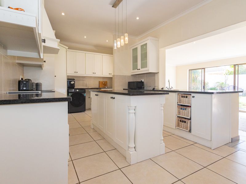 A well-appointed kitchen featuring a central island with granite countertops, ample white cabinetry, recessed lighting, and tiled flooring, with an open flow to the outdoors.