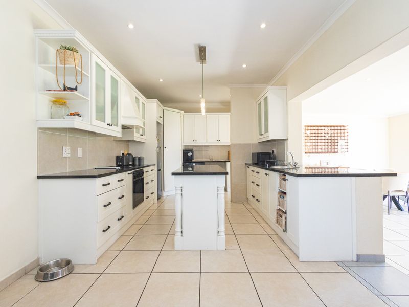A bright, modern kitchen featuring white cabinetry, granite countertops, a central island, and tiled flooring, offering a clean and functional workspace.