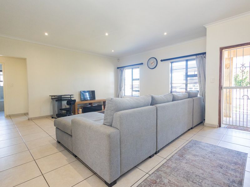 A spacious living room featuring neutral tiled flooring, recessed downlighting, and direct access to the exterior via a secure entrance door.