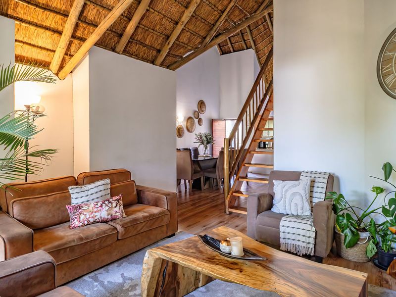 Open-plan living area featuring a high vaulted thatched ceiling with exposed timber rafters, timber flooring, and a wooden staircase leading to the upper level.