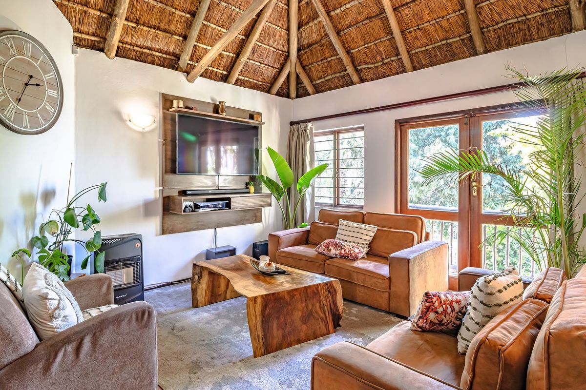 A cozy living room featuring a high vaulted thatched ceiling with exposed timber rafters, built-in media unit, and large glass doors leading outdoors.