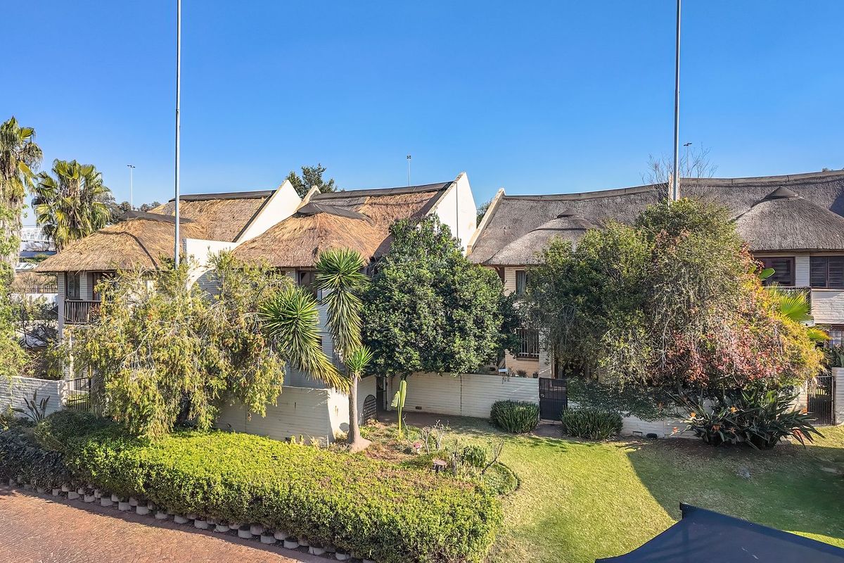 Rear view of the apartment complex featuring traditional thatched roofing, established garden landscaping, and a paved driveway area.
