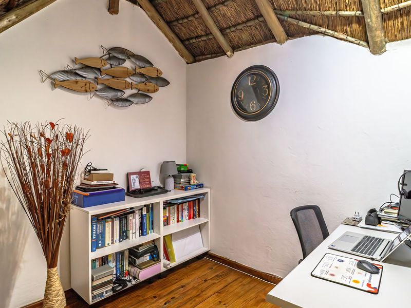 A cozy home office featuring exposed thatch roofing with timber rafters and warm hardwood flooring, creating a rustic and inviting workspace.