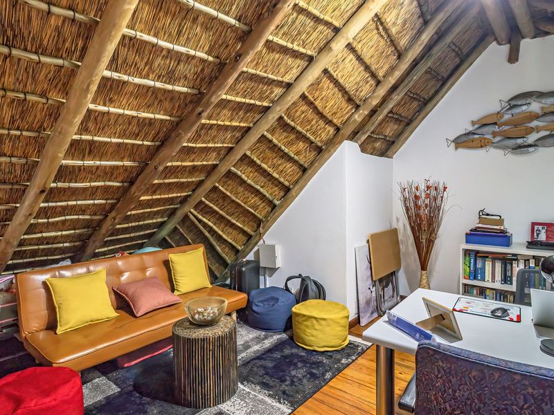 A cozy attic-style office space featuring exposed timber rafters, a traditional thatched roof, and warm timber flooring.