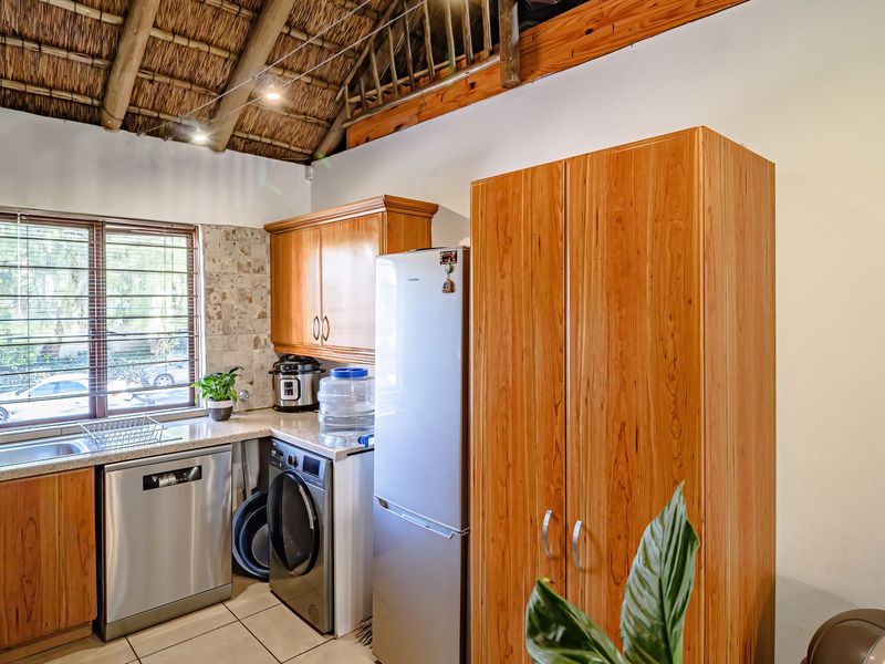 Kitchen featuring wooden cabinetry, tiled backsplash, and a unique exposed thatched roof ceiling with timber beams.
