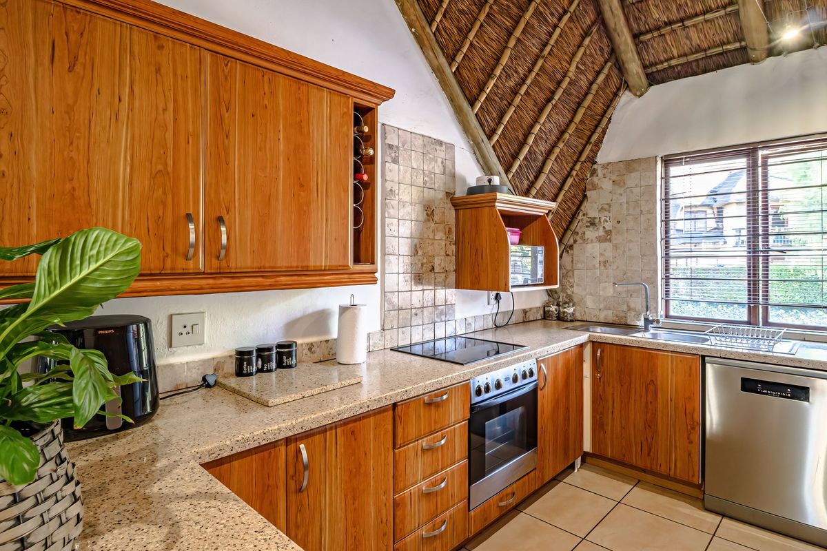 A functional kitchen featuring wooden cabinetry, granite countertops, built-in oven and hob, tiled backsplash, and a unique vaulted thatch roof ceiling.