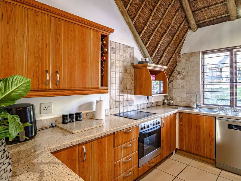 A functional kitchen featuring wooden cabinetry, granite countertops, built-in oven and hob, tiled backsplash, and a unique vaulted thatch roof ceiling.