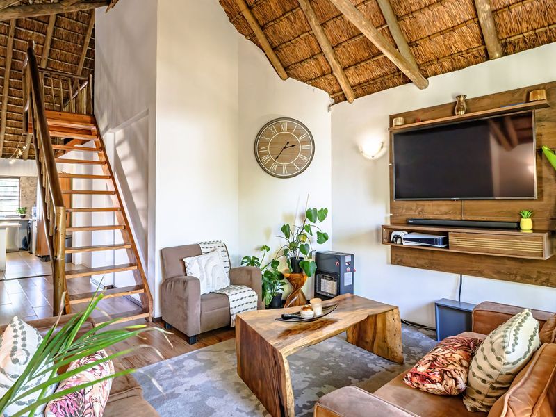 Open-plan living area featuring a high thatched ceiling with exposed timber rafters, a wooden staircase, and a built-in media console.