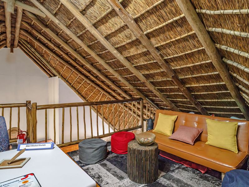 A cozy loft-style living area featuring a traditional thatched roof with exposed timber rafters and a rustic wooden balustrade.