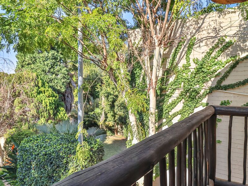 A balcony featuring a rustic timber balustrade and a painted brick wall, overlooking a lush, tree-filled garden area.