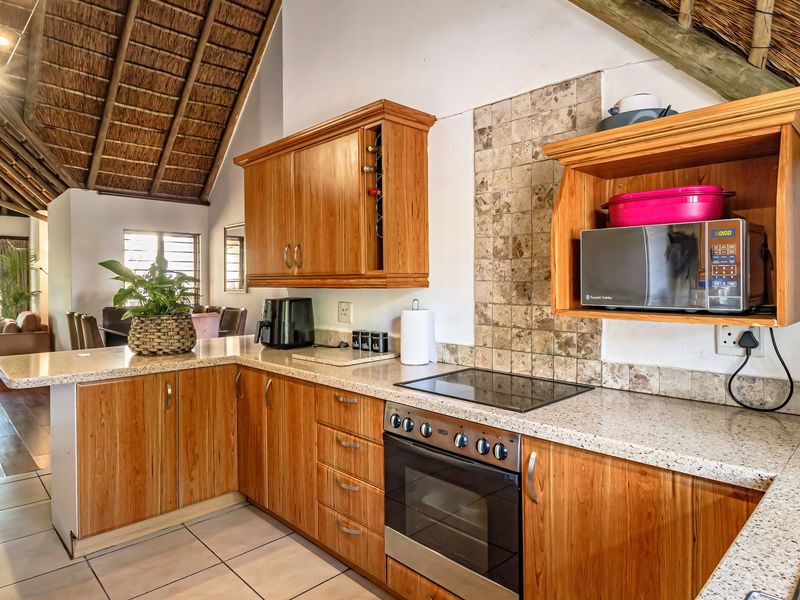 Kitchen featuring wooden cabinetry, granite countertops, built-in oven, and electric hob, set under a unique exposed thatch roof structure.