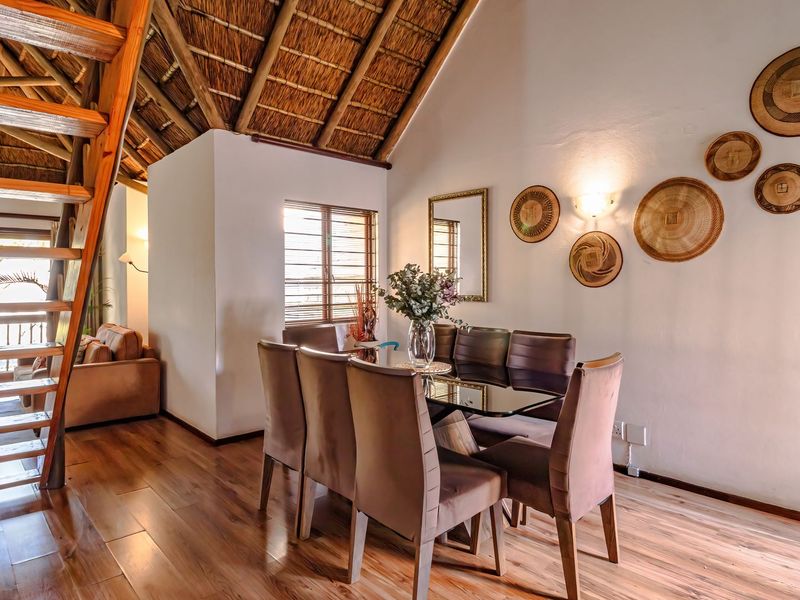Open plan dining area featuring a striking thatched roof with exposed timber rafters, timber staircase, and warm laminate flooring.