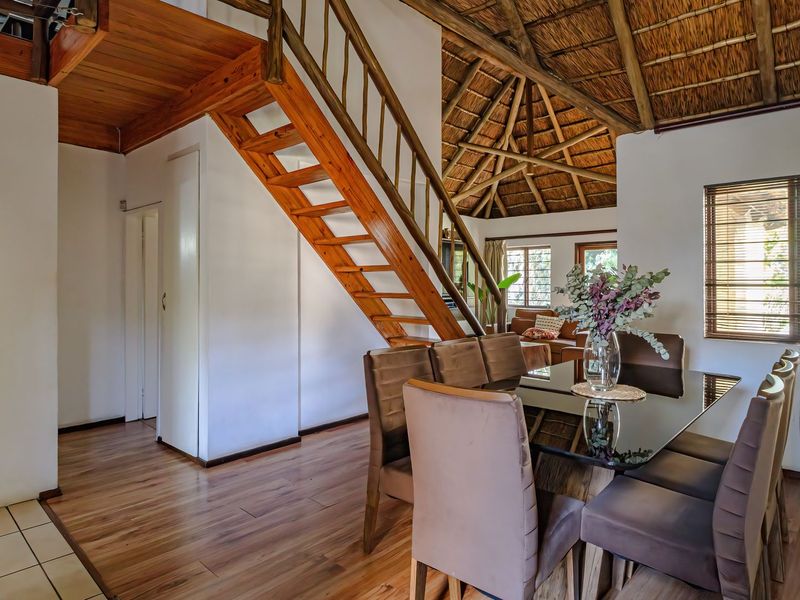 Open plan living and dining area featuring a distinctive thatched roof with exposed timber rafters and a wooden staircase leading to an upper level.