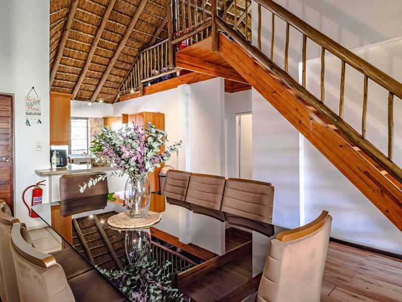 Open plan living and dining area featuring a high thatched ceiling, wooden staircase, and tiled flooring, creating a warm and rustic atmosphere.