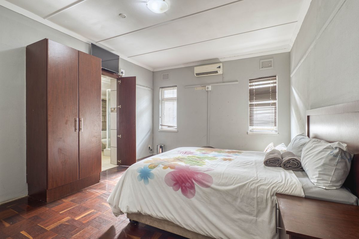 A bedroom featuring parquet flooring, a built-in wardrobe, and a wall-mounted air conditioning unit, with an adjoining en-suite bathroom.