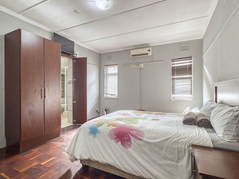 A bedroom featuring parquet flooring, a built-in wardrobe, and a wall-mounted air conditioning unit, with an adjoining en-suite bathroom.