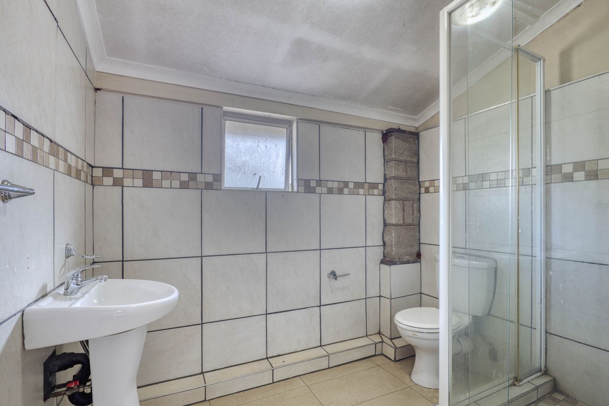 A functional bathroom featuring a pedestal basin, toilet, and shower enclosure, currently requiring maintenance and cosmetic updates to the tiling and ceiling finishes.