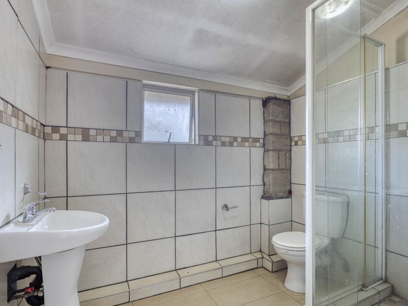 A functional bathroom featuring a pedestal basin, toilet, and shower enclosure, currently requiring maintenance and cosmetic updates to the tiling and ceiling finishes.