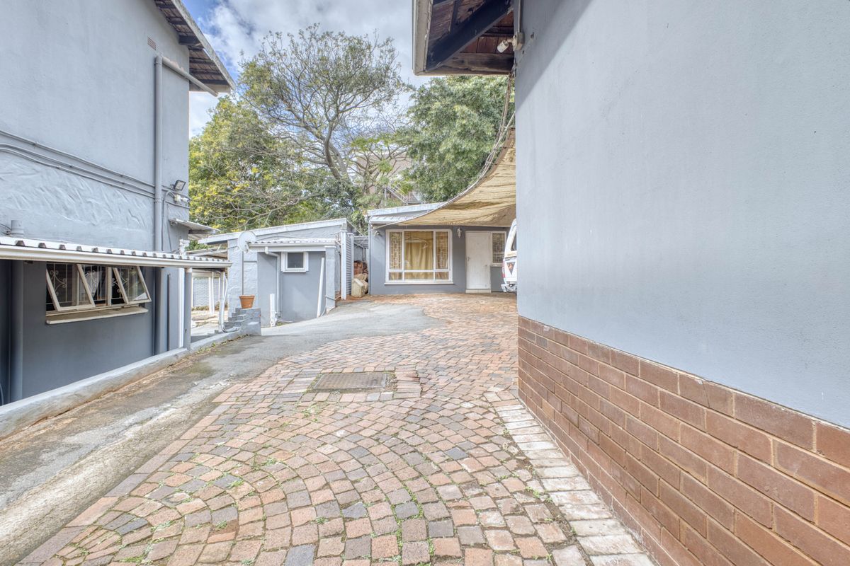 A paved rear courtyard area featuring a shade sail, connecting multiple sections of the lodge building with brick and plastered wall finishes.