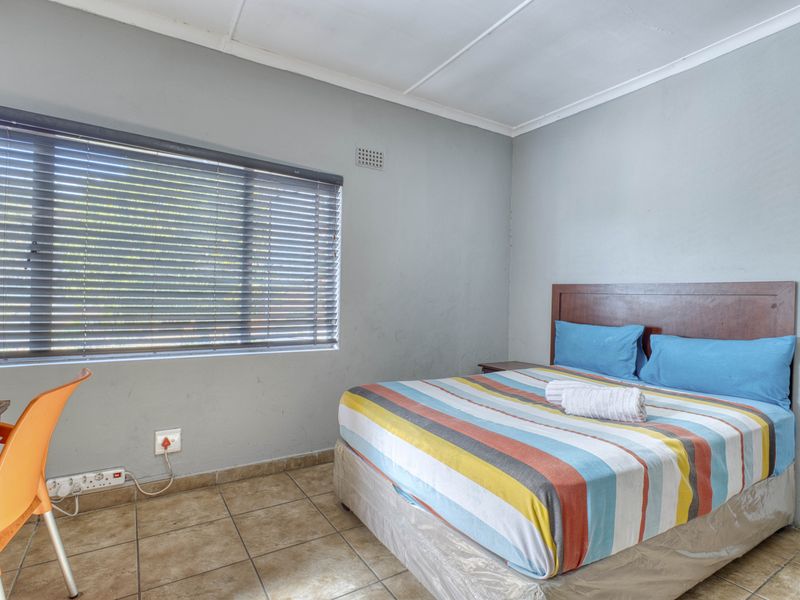 A functional bedroom featuring tiled flooring, neutral wall finishes, and venetian blinds, providing a simple and practical living space.