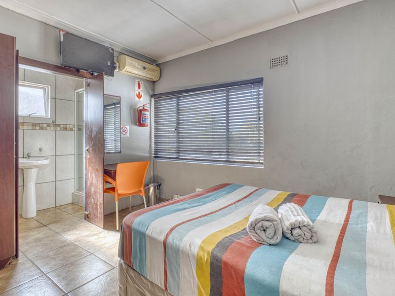 A functional bedroom featuring an en-suite bathroom with a pedestal basin and shower, equipped with a wall-mounted air conditioner and venetian blinds.