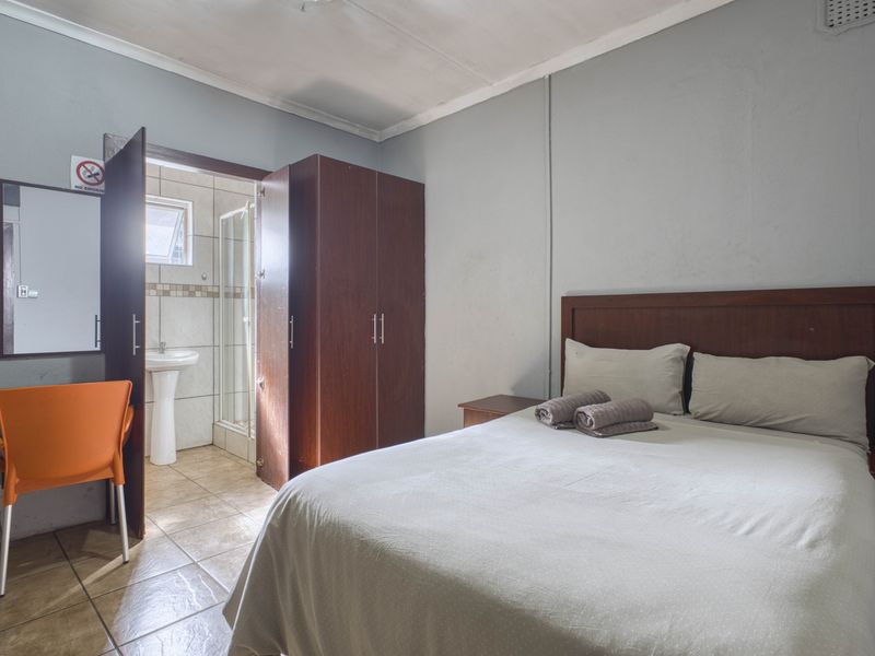 A bedroom featuring an en-suite bathroom with a shower and pedestal basin, complemented by built-in wardrobe storage and tiled flooring.
