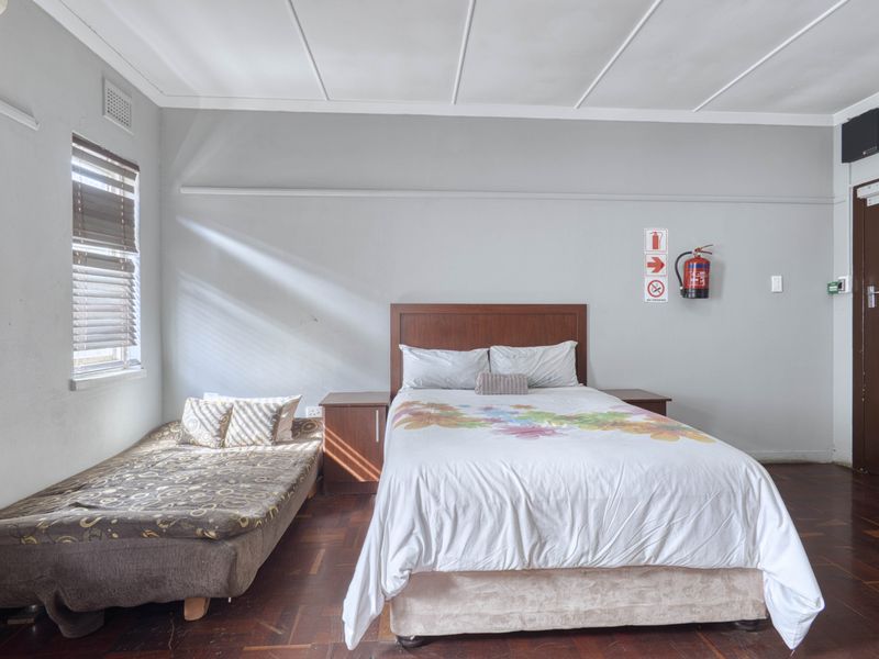 A functional bedroom featuring parquet flooring, venetian blinds, and essential safety equipment including a wall-mounted fire extinguisher.